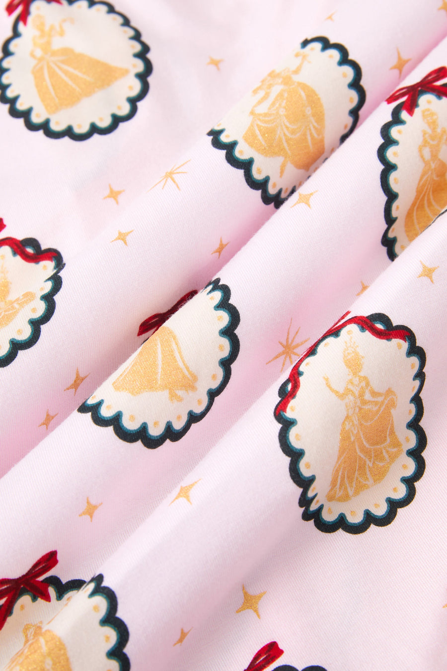 An all-over print featuring rows of scalloped medallions with a dark green border, gold dots, and a thin red bow at the top, over a pale pink background color called Sakura. One row of medallions alternates gold silhouettes of Cinderella holding her glass slipper, and Snow White with a bird on her finger. Another row of medallions alternates gold silhouettes of Belle holding her skirt and a rose, and Tiana holding her skirt.