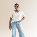 Smiling woman standing in front of a beige background while modeling the Women's Relaxed Fit V-Neck in Pastel Mickey Mouse 
