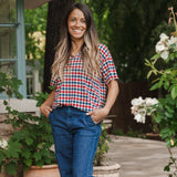 Model standing in front of greenery while wearing the  Women's Relaxed Fit V-Neck in Patriotic Gingham paired with dark denim 