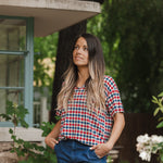Model standing outside looking upwards while wearing the Women's Relaxed Fit V-Neck in Patriotic Gingham with hands in her jean pockets 