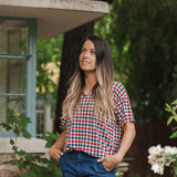 Model standing outside looking upwards while wearing the Women's Relaxed Fit V-Neck in Patriotic Gingham with hands in her jean pockets 