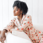 Woman sitting on a cream chair wearing long sleeve button up pajamas in a peach print