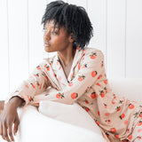 Woman sitting on a cream chair wearing long sleeve button up pajamas in a peach print