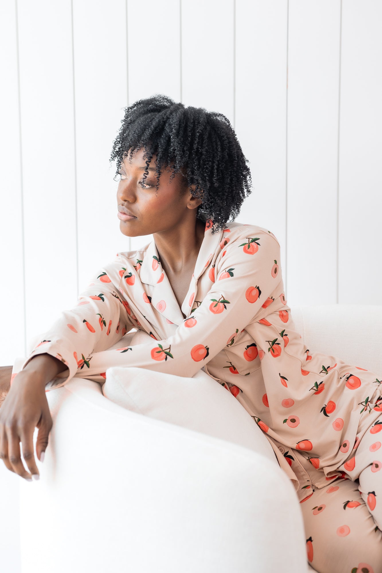 Woman sitting on a cream chair wearing long sleeve button up pajamas in a peach print
