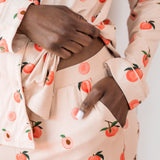 Woman wearing long sleeve button up pajamas in a peach print showing waistband and pocket detail of pant