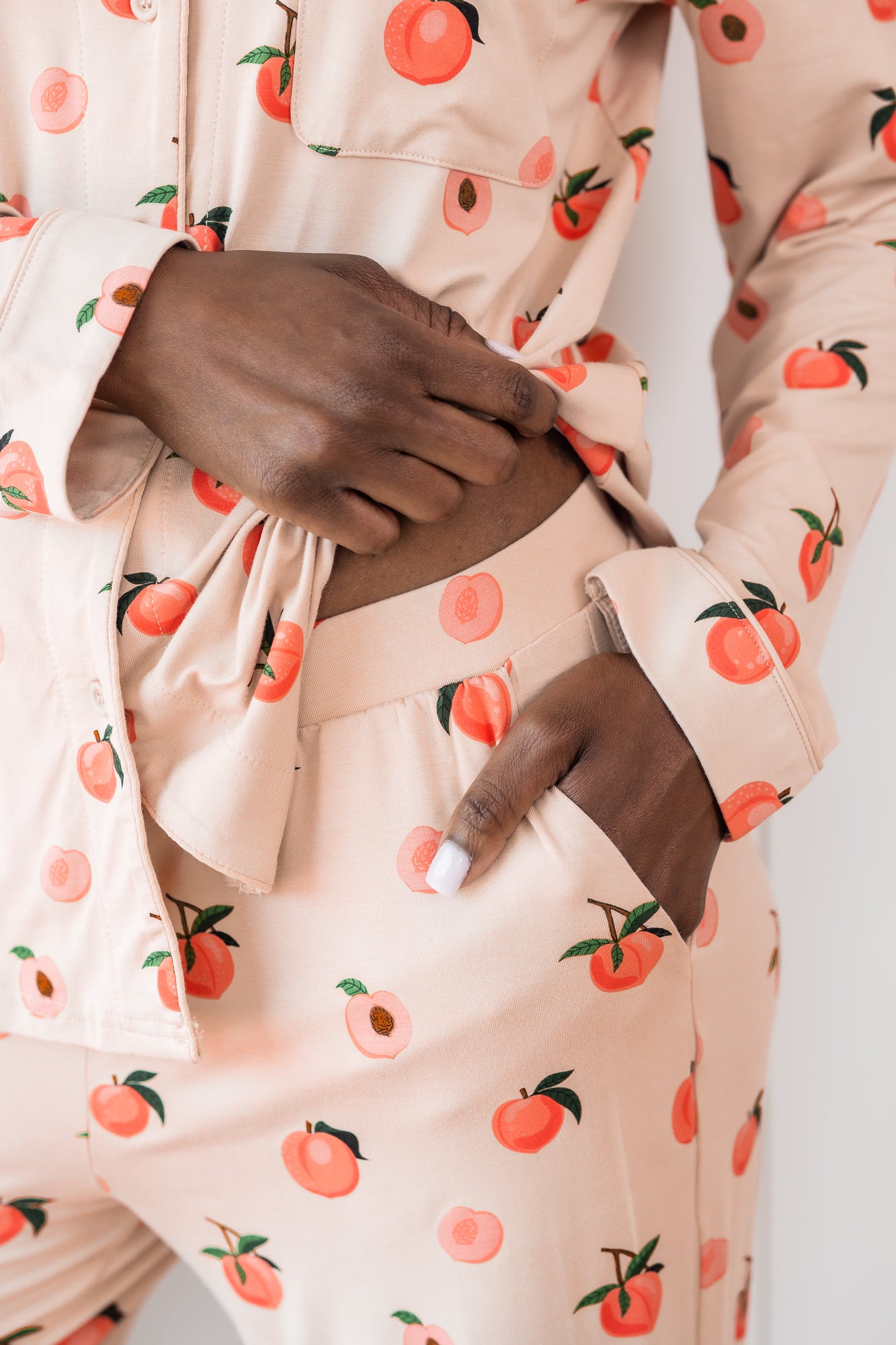 Woman wearing long sleeve button up pajamas in a peach print showing waistband and pocket detail of pant