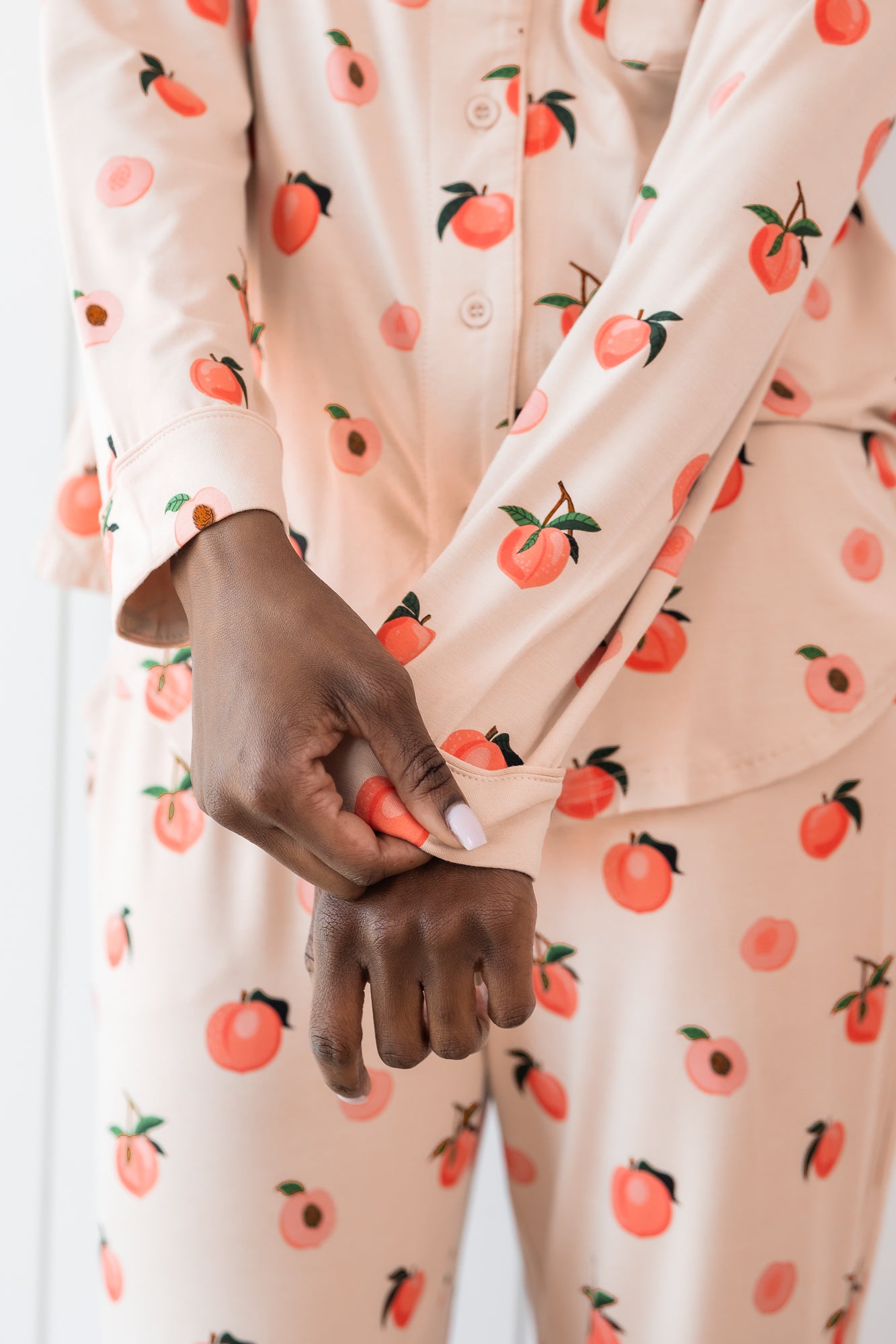 Woman wearing long sleeve button up pajamas in a peach print showing cuff of top