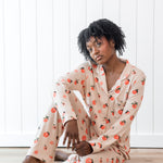 Woman sitting on wood floor wearing long sleeve button up pajamas in a peach print