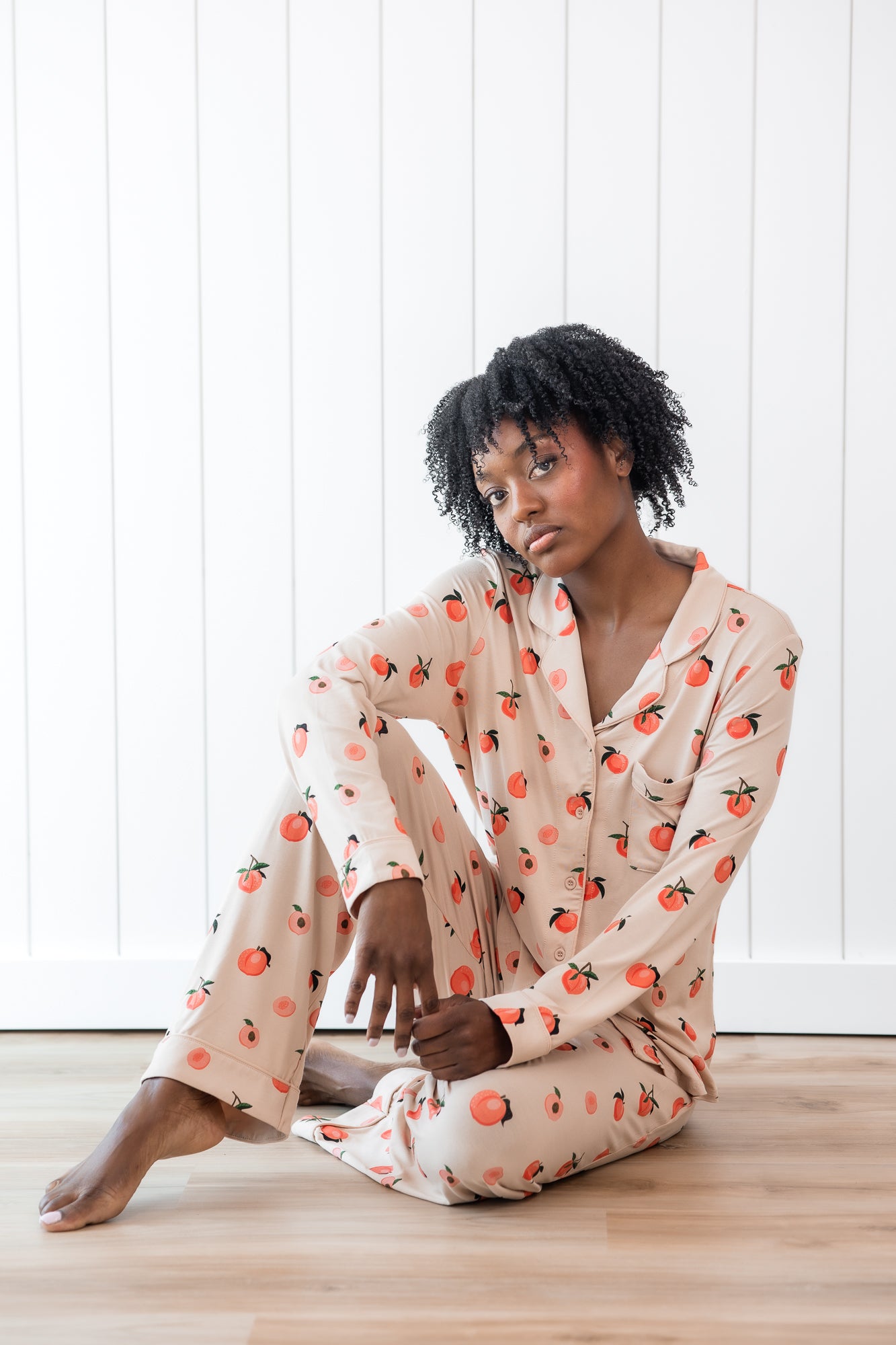 Woman sitting on wood floor wearing long sleeve button up pajamas in a peach print