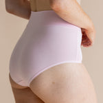 Person wearing light pink high-waisted underwear on a beige background