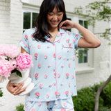 Woman outside smiling down holding a vase of flowers and pushing back her hair in short sleeve pajamas and shorts in Peony on Breeze. ---1615 1