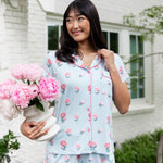 Woman outside soft smiling holding a vase of flowers touching her collar in short sleeve pajamas and shorts in Peony on Breeze print.  ---PJ 2