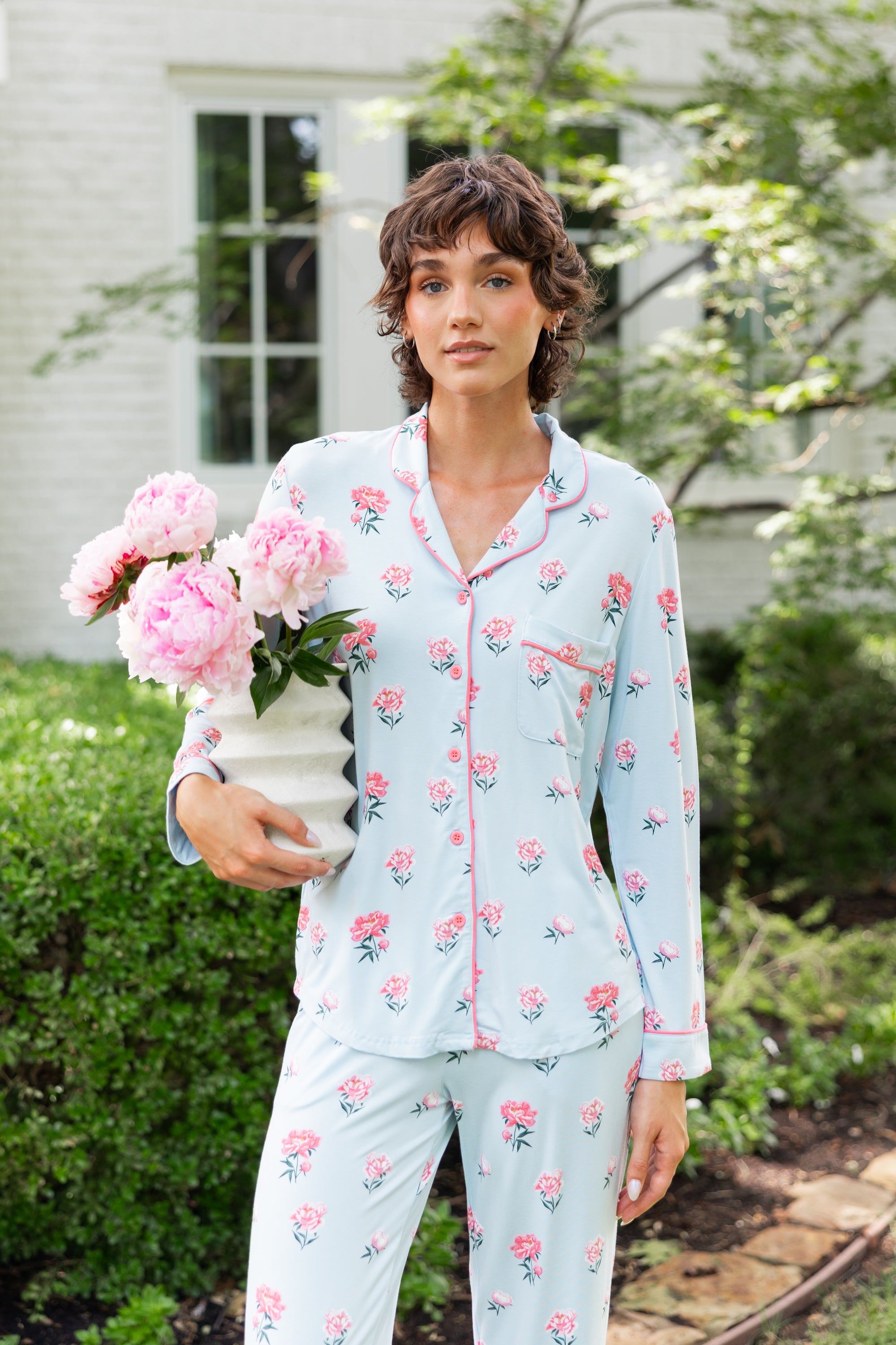 Woman outside soft smiling holding a vase of flowers in long sleeve pajamas and pants in Peony on Breeze print. ---PJ 4