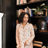 Woman in gilmore girl printed pajamas standing in front of a bookshelf with decorative items.