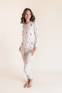 A woman modeling a two-piece long-sleeve pajama set with a colorful pickleball print on a light cream background, set against a solid warm beige studio backdrop.
