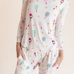 A woman wearing a matching long-sleeve pajama top and pants set with a colorful pickleball print on a white background, photographed against a plain light beige studio backdrop.