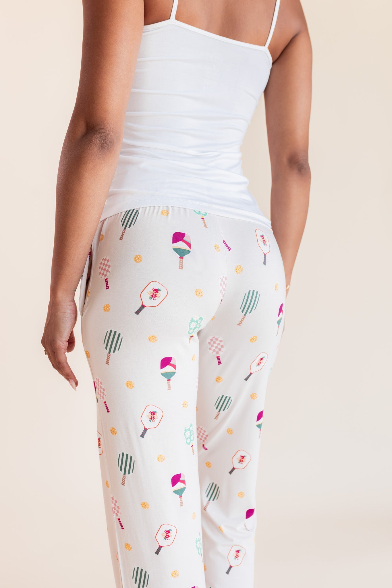 White leggings with a colorful pickleball racket pattern, worn by a model from the back against a light beige background.