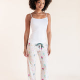 A woman modeling a two-piece pajama set consisting of a white camisole top and white pants with a colorful pickleball  print, set against a solid cream background.