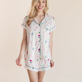 A woman modeling a short-sleeve pajama shirt and matching shorts set with a multicolor pickleball print on a warm off-white background, set against a solid beige studio backdrop.
::: Model is 5'9" wearing size XS ///
---PJ 2