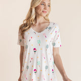 A woman modeling a white short-sleeve V-neck top with a colorful pickleball print, paired with white pants, against a solid beige background.
::: Model is 5'9" wearing size XS ///