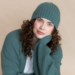 Modal wearing Chunky Knit Adult Ribbed Beanie in pine over white t-shirt and chunky knit women's cardigan in pine and blue jeans on a beige background