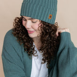 Modal wearing Chunky Knit Adult Ribbed Beanie in pine over white t-shirt and chunky knit women's cardigan in pine on a beige background