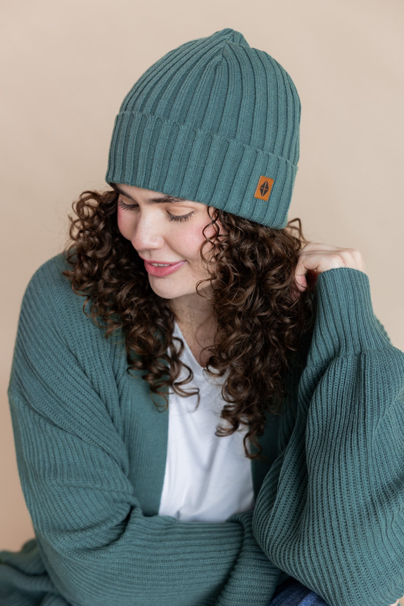 Modal wearing Chunky Knit Adult Ribbed Beanie in pine over white t-shirt and chunky knit women's cardigan in pine on a beige background