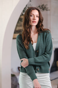 Woman with one arm holding the other in a cardigan in pine color