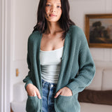 Modal standing in living room wearing Chunky Knit Women's Waffle Cardigan in Pine over white camisole and blue jeans
::: Model is 5'10" wearing size S ///