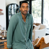 Male model wearing muted sage green button up long sleeve pajamas in a living room