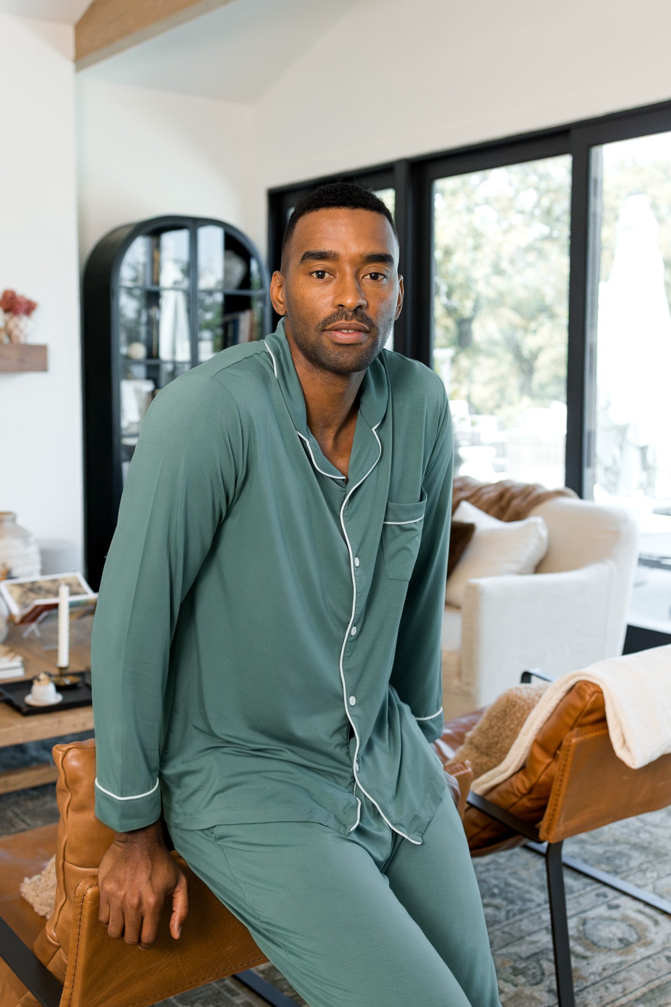Male model wearing muted sage green button up long sleeve pajamas in a living room