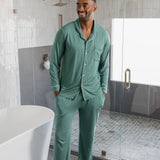 Male model wearing muted sage green button up long sleeve pajamas in a luxury bathroom