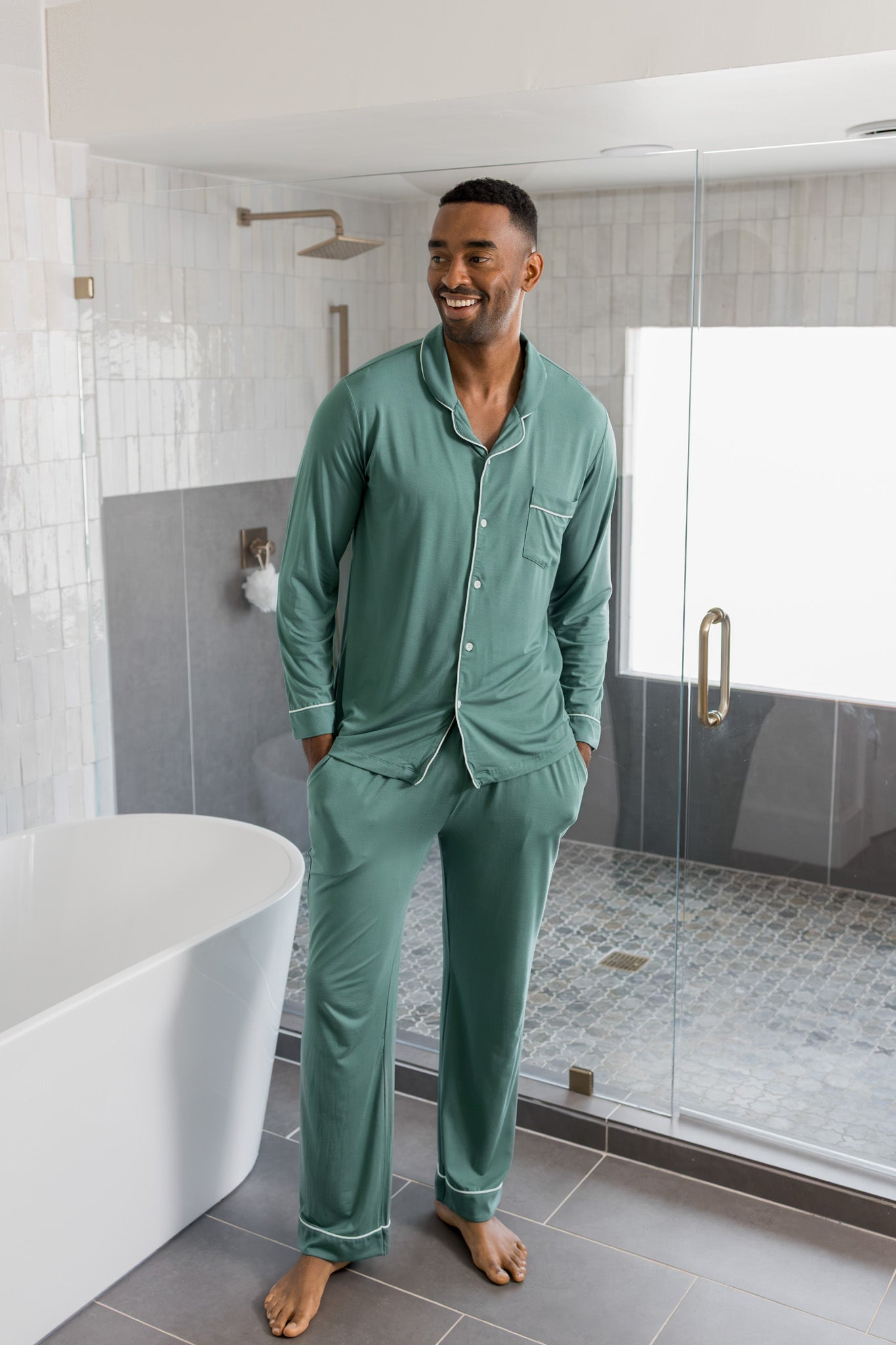 Male model wearing muted sage green button up long sleeve pajamas in a luxury bathroom