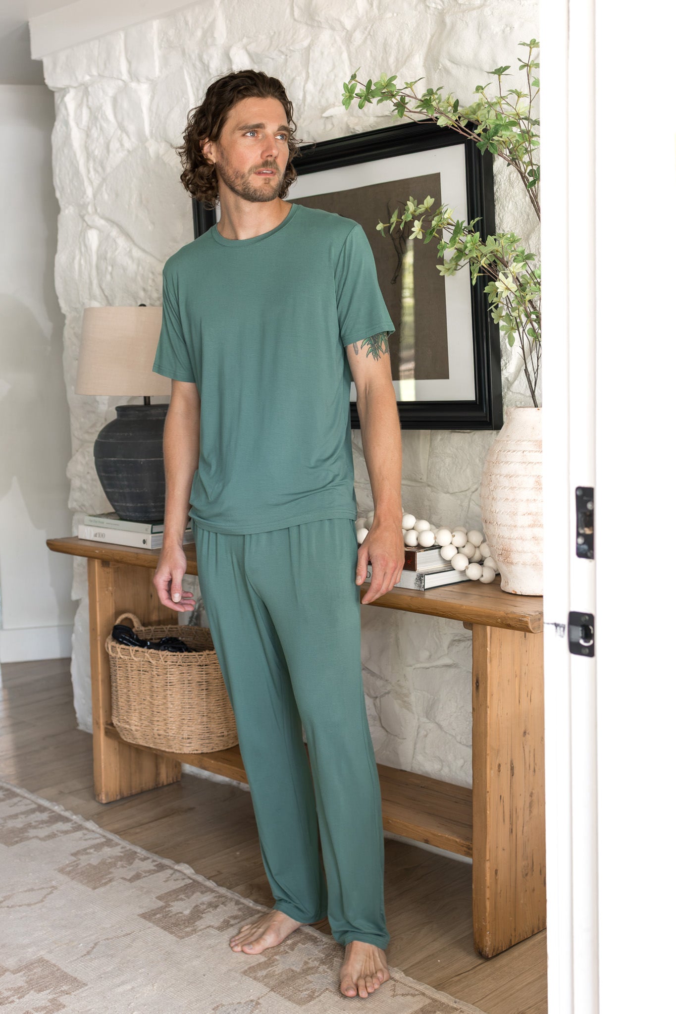 Male model wearing a pine green crew neck tee and matching lounge pants in a living room