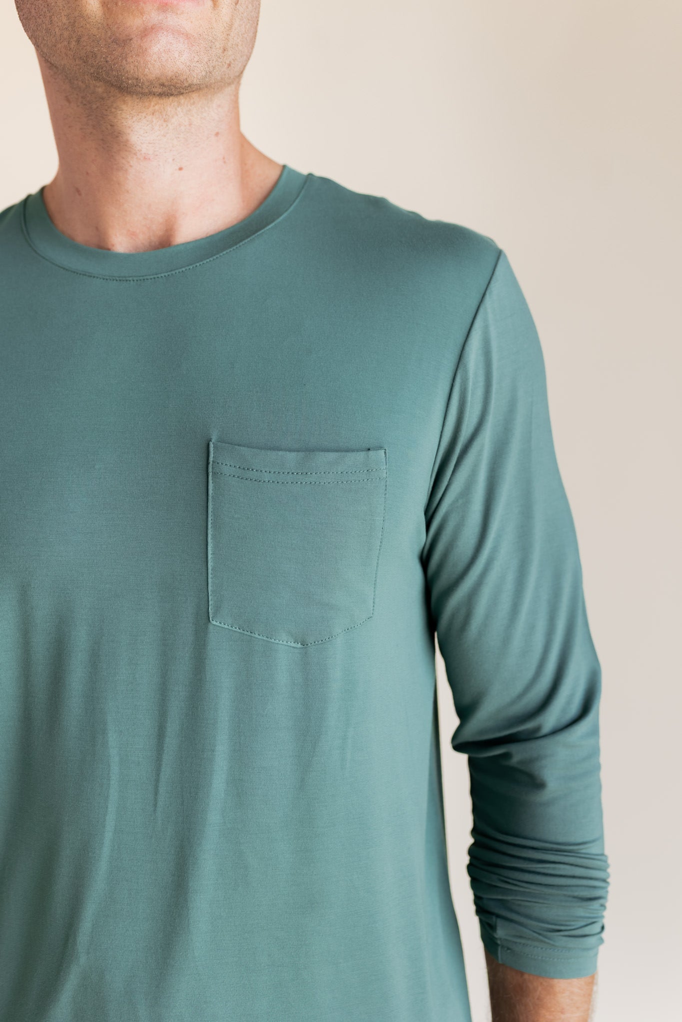 Male model wearing muted sage green jogger set in a studio setting, close up on pocket detail on top