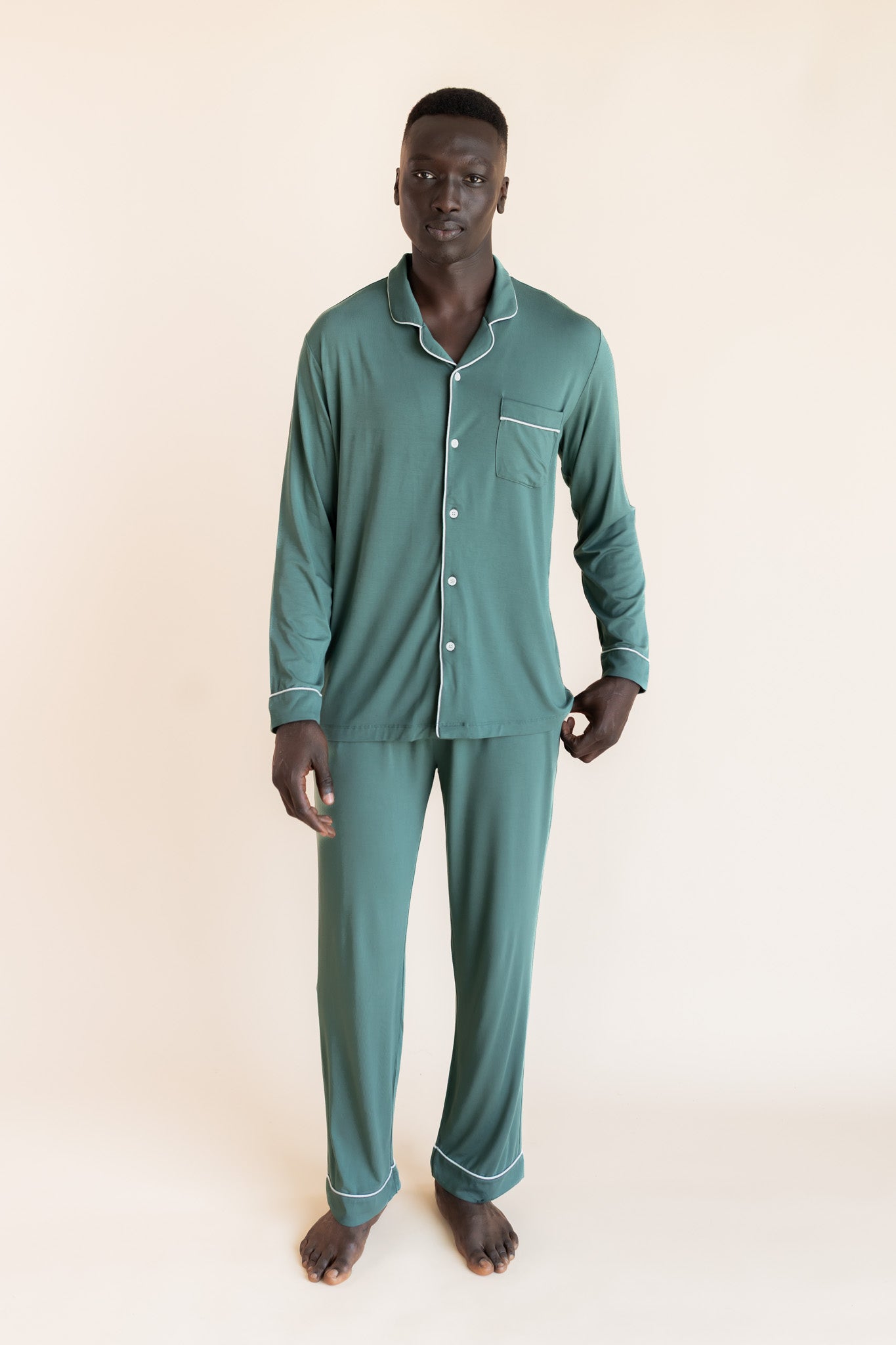 Male model wearing muted sage green button up long sleeve pajamas in a studio setting