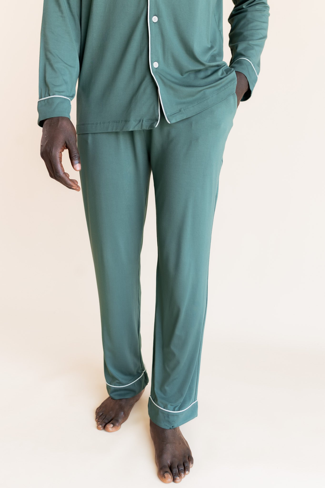 Male model wearing muted sage green button up long sleeve pajamas in a studio setting, close up on pant