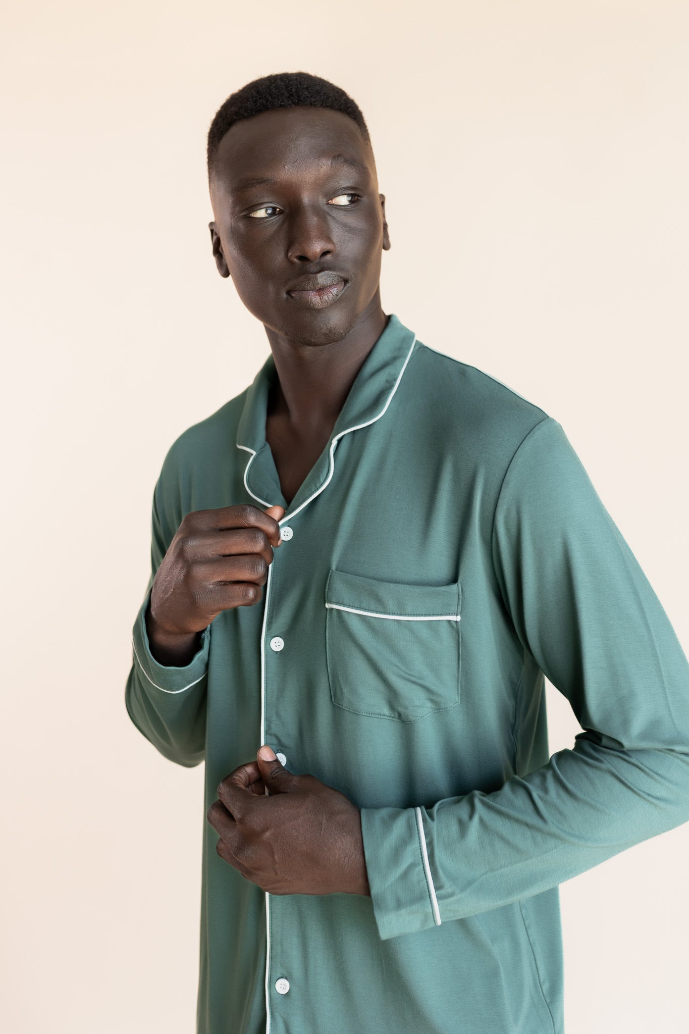 Male model wearing muted sage green button up long sleeve pajamas in a studio setting, close up on buttons