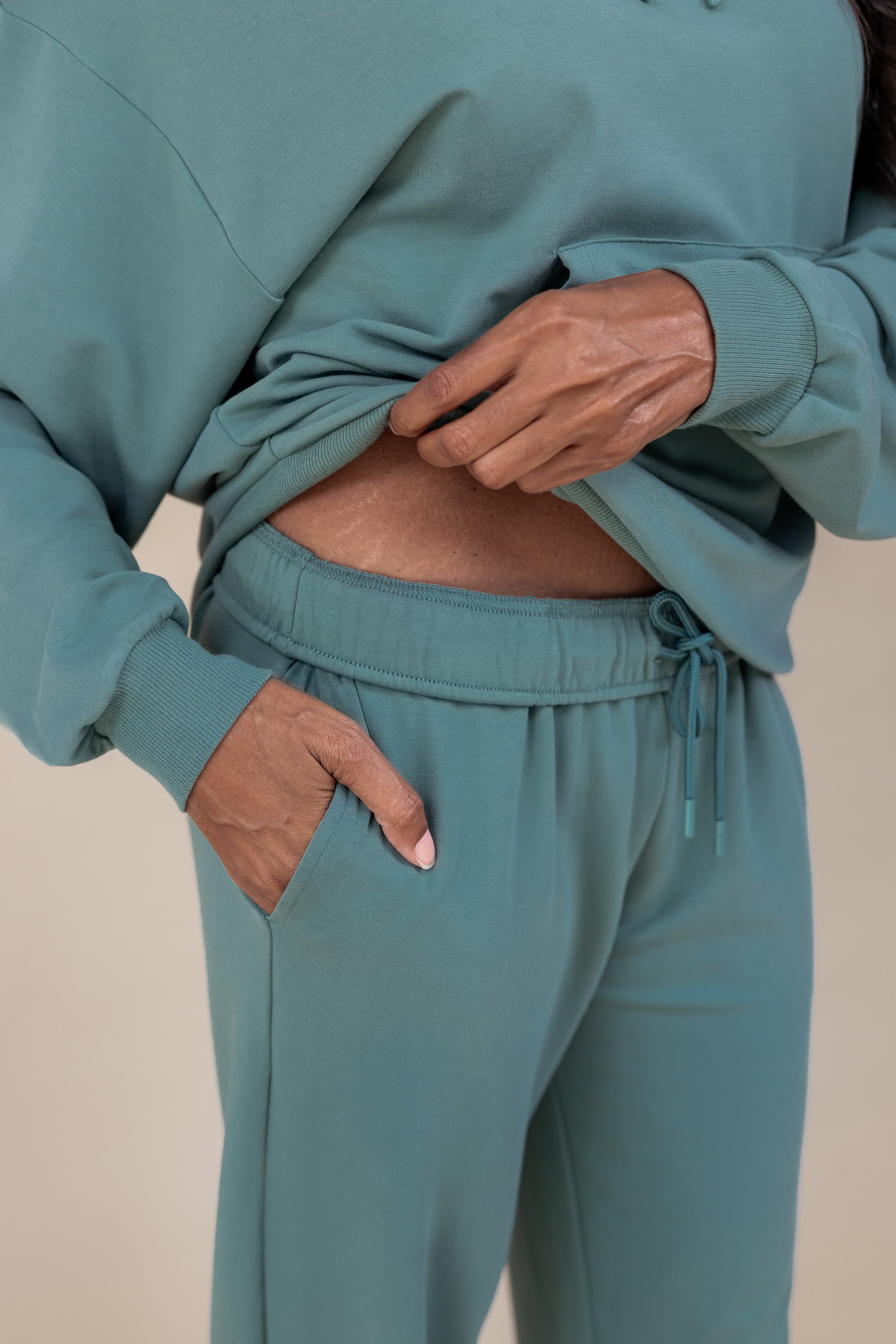 Modal showcasing the pockets on Women's Jogger Pants in Pine color under similar color women's hoodie on a beige background