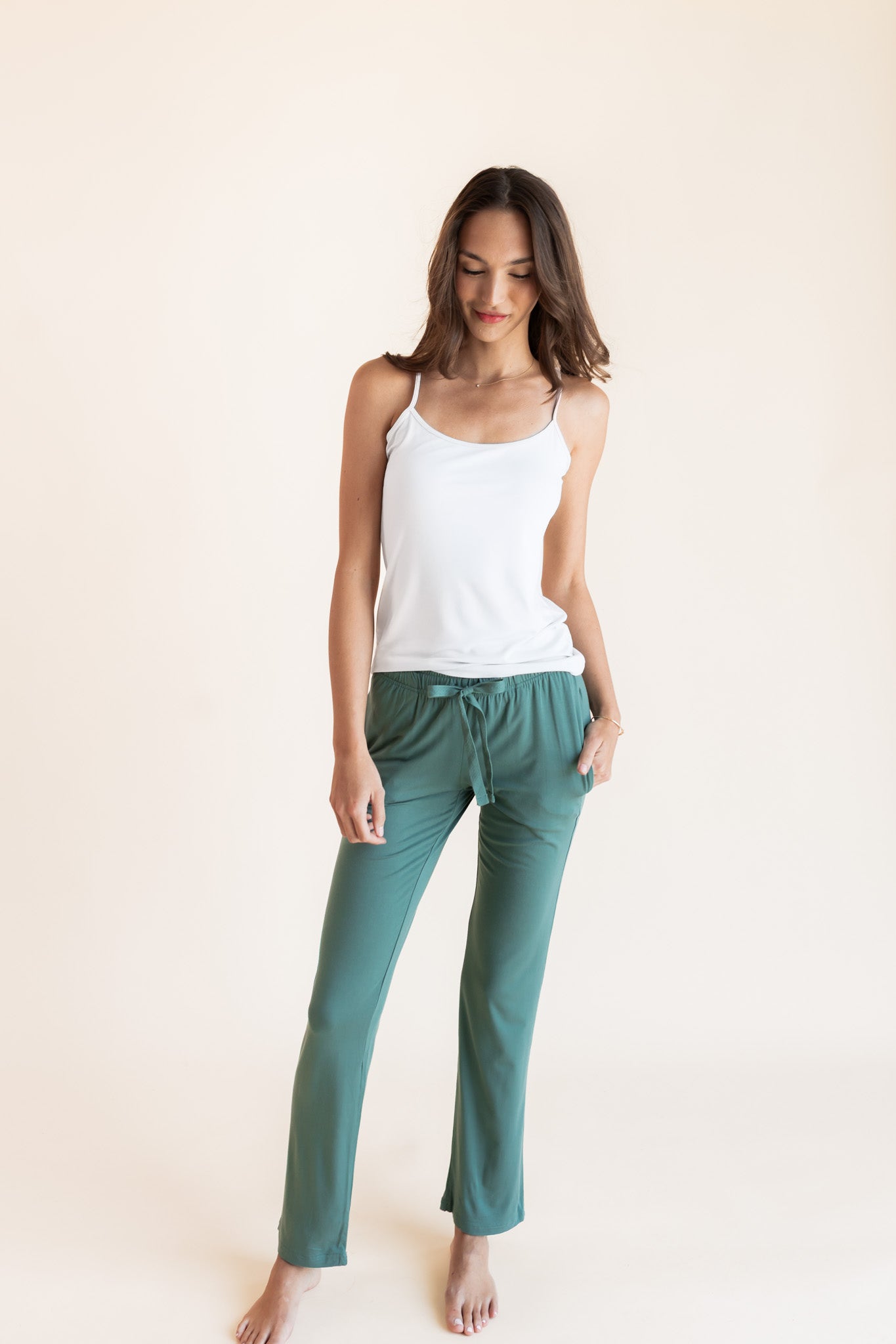Model wearing Women's Lounge Pants in Pine under white camisole on a beige background
