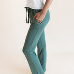 Model showcasing pockets on Women's Lounge Pants in Pine under white camisole on a beige background