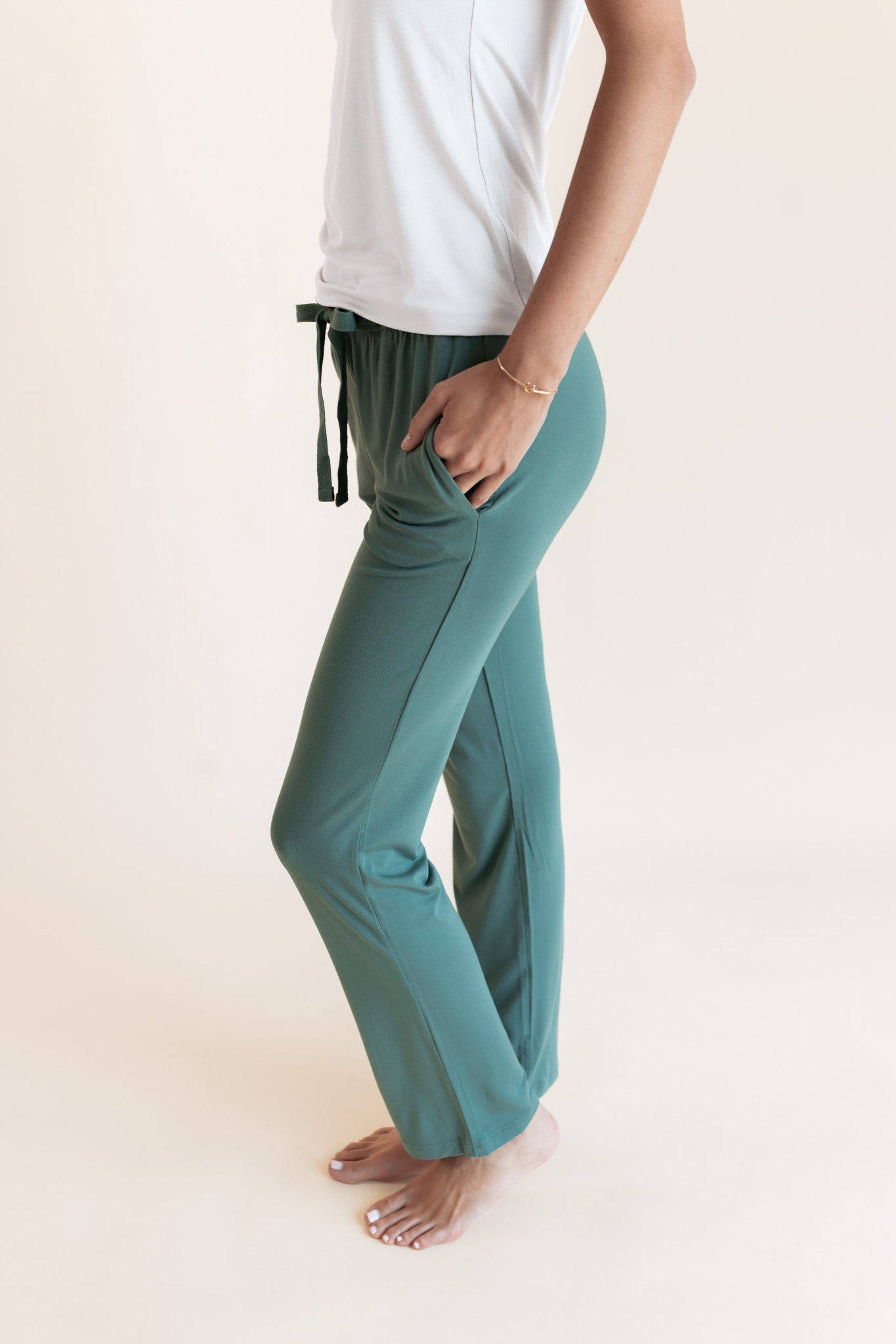Model showcasing pockets on Women's Lounge Pants in Pine under white camisole on a beige background