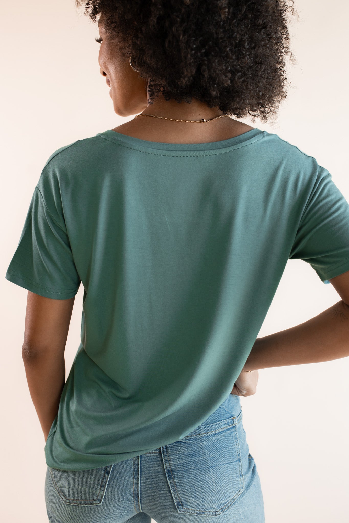 Woman modeling a green v-neck oversized tee, showing back of shirt