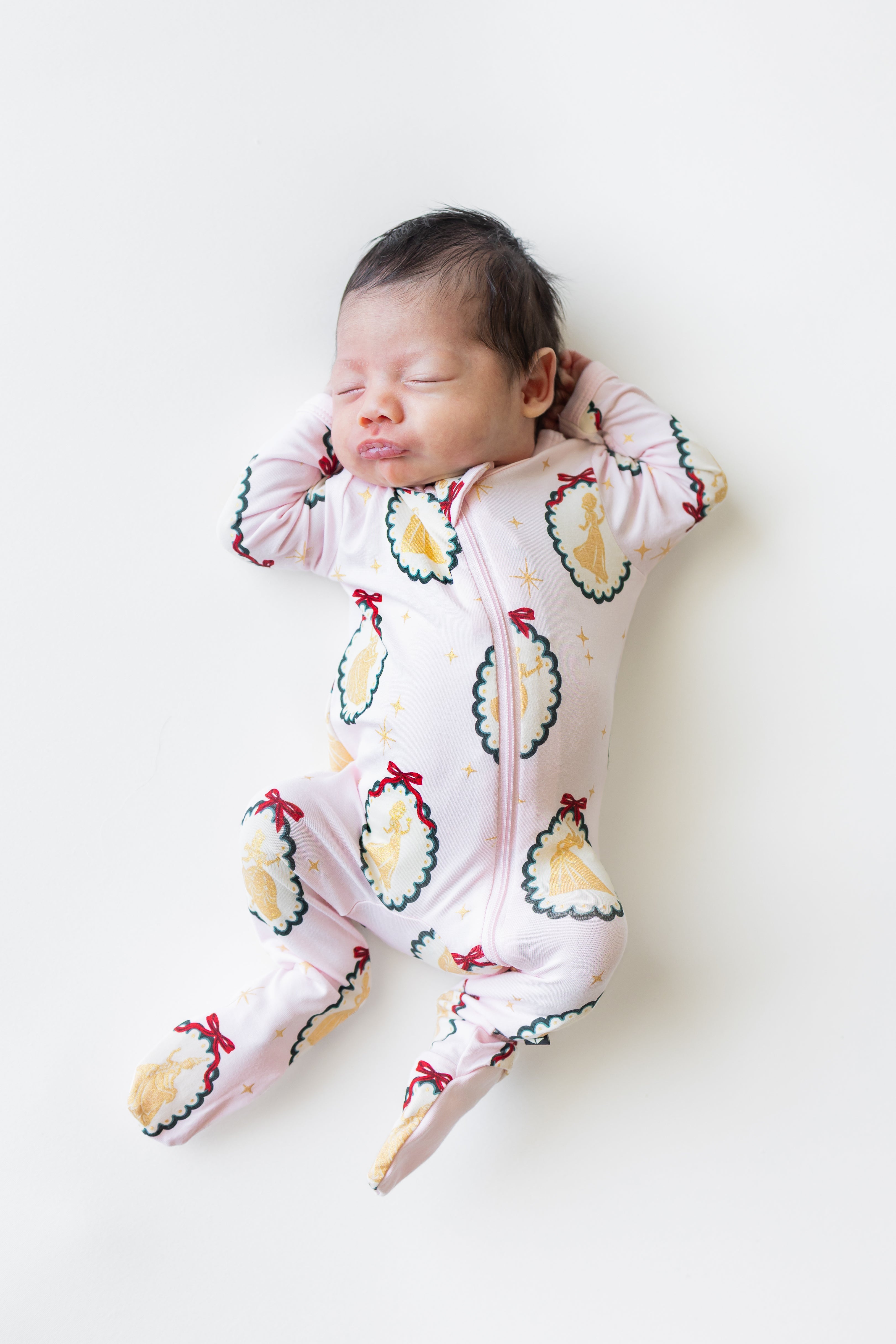 Baby sleeping in Zippered Footie in Princess Holiday Portraits print on a beige background