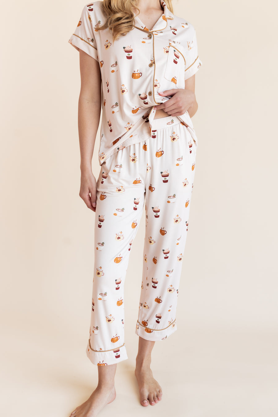 Model showcasing the front side of pajamas of Women's Short Sleeve Cropped Pajama Set in Pumpkin Spice Latte print on a beige background