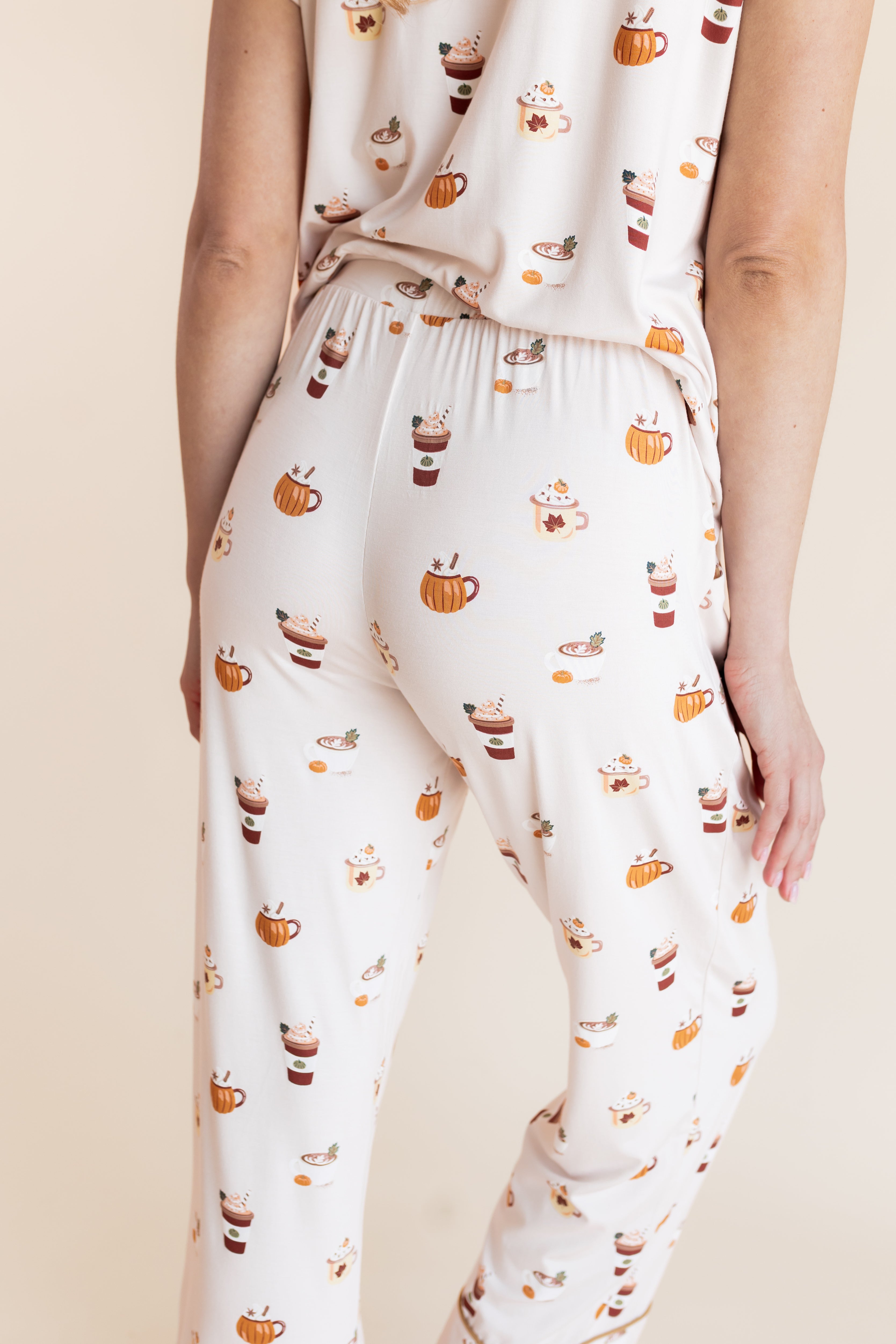 Model showcasing the backside of Women's Short Sleeve Cropped Pajama Set in Pumpkin Spice Latte print on a beige background