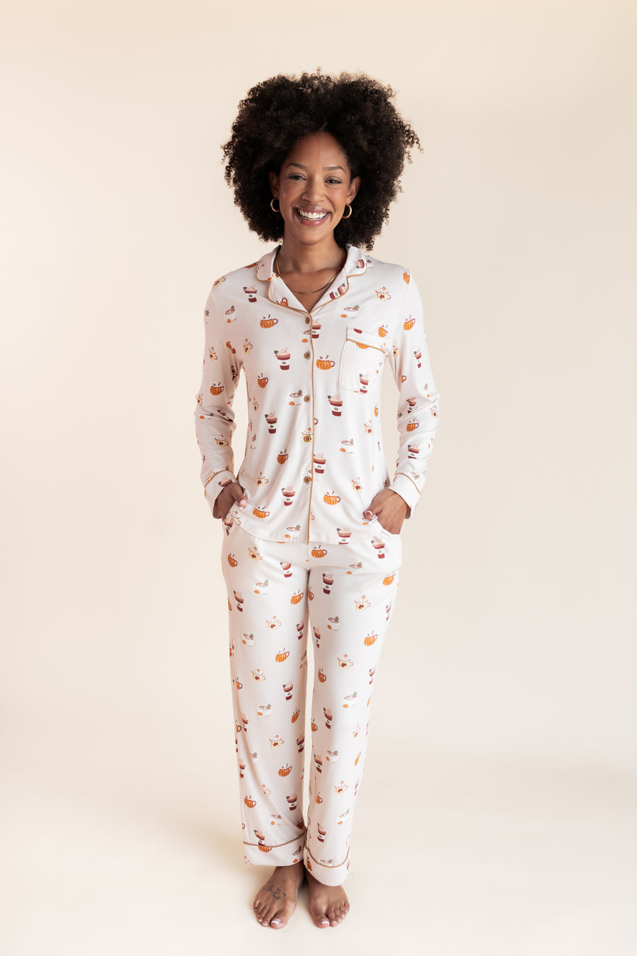 Model smiling in Long-Sleeved Women's Pajama Set in Pumpkin Spice Latte print on a beige background