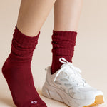 Model wearing Adult Scrunch Socks in Ruby and a white sneaker on one foot on a beige background