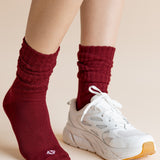 Model wearing Adult Scrunch Socks in Ruby and a white sneaker on one foot on a beige background