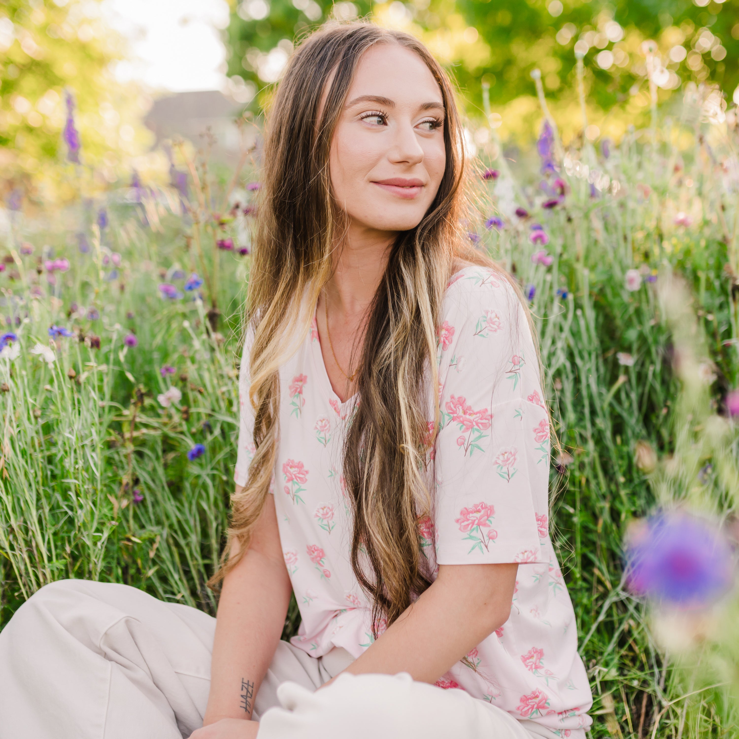 Woman sitting in a wildflower field wearing  Women's Relaxed Fit V-Neck in Sakura Peony 